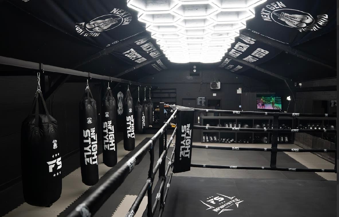 The gym floor seen from inside the ring, bags and kit shelving along the wall