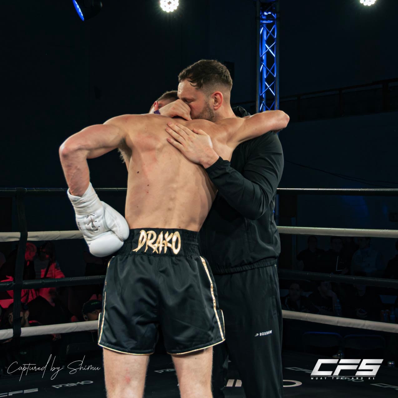 A Next Gen fighter and his coach embracing in the ring after the fight