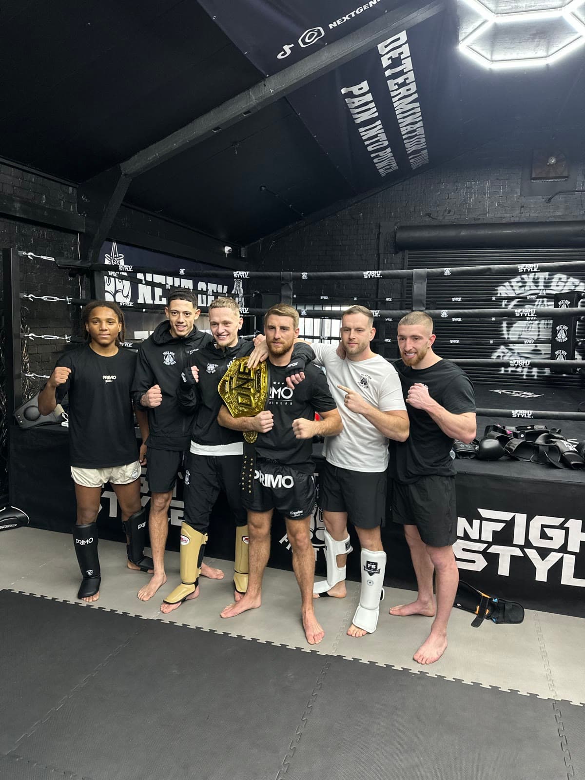 Members of the Next Gen team in the gym with a championship belt