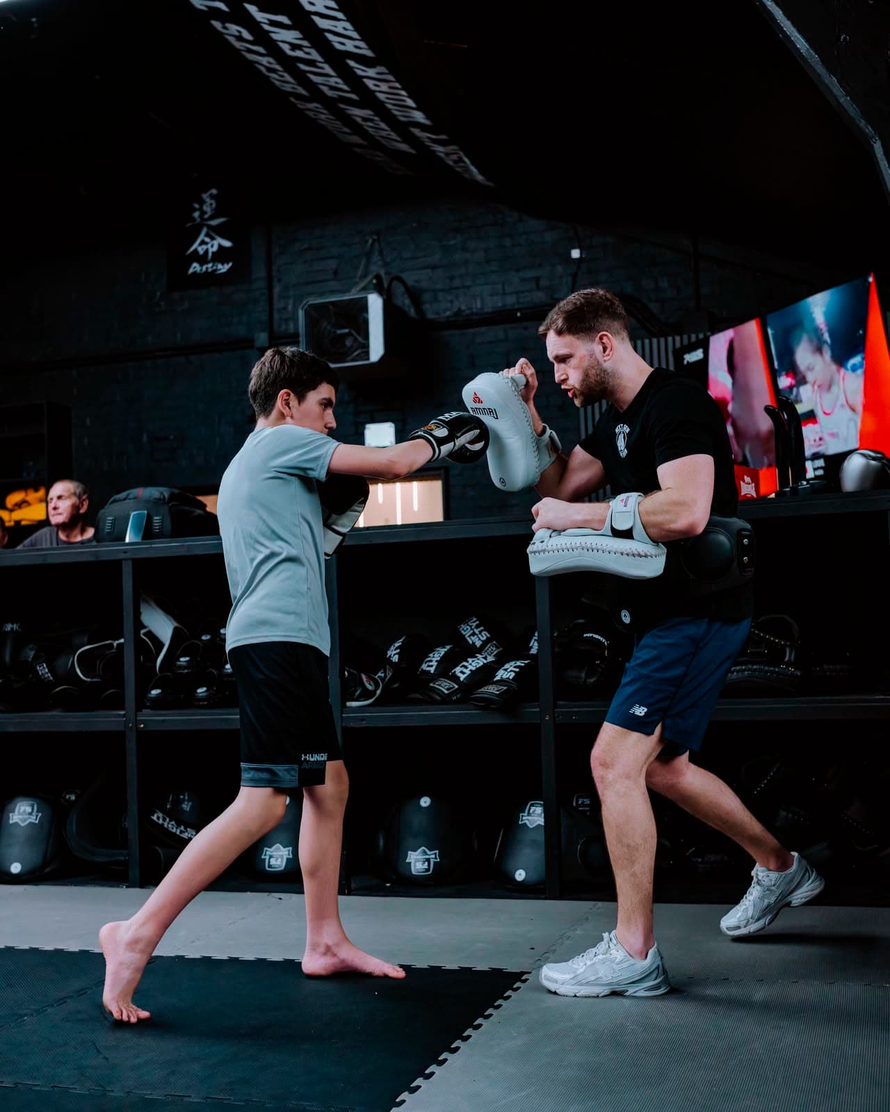 Head coach Hayden holding the mitts and belly pad for a junior member on the gym floor
